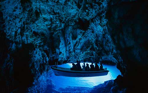 Cueva Azul de Bi&scaron;evo iluminada de azul, con un bote y visitantes